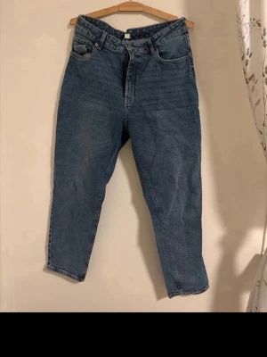 Blå mom jeans med hög midja - Snygga blå mom jeans med hög midja och klassisk femficksdesign. Jeansen har raka ben och stängs med dragkedja och knapp. 