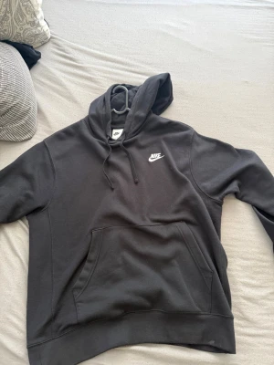 Svart Nike hoodie med logga - Svart hoodie från Nike med vit broderad logga på bröstet. Klassisk modell med huva och dragsnören samt stor magficka framtill. Mjuk och skön bomullsblandning, perfekt för en avslappnad streetstyle-look.