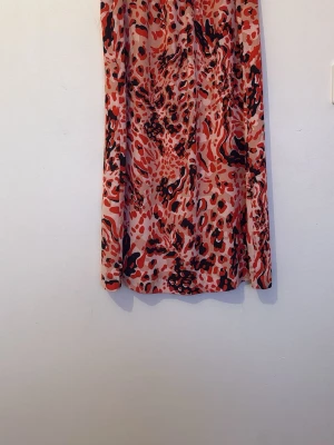 Röd leopardmönstrad klänning - Snygg kortklänning med leopardmönster i rött, svart och beige. Klänningen har långa ärmar och en lös passform, perfekt för dig som vill sticka ut. Tillverkad i ett lätt och mjukt polyestertyg som känns skönt mot huden.