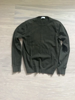 Mörkgrön stickad tröja Tiger of Sweden - Snygg mörkgrön stickad tröja från Tiger of Sweden med rund halsringning och ribbade muddar vid ärmslut och nederkant. Tröjan har en klassisk passform och är tillverkad i mjukt material som passar perfekt till lager på lager.