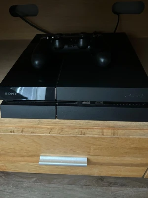 PlayStation 4 - Säljer en svart PlayStation 4 från Sony med tillhörande svart DualShock 4-handkontroll. Och 2 spel. Konsolen har en stilren, rektangulär design i plast med matta och blanka ytor. Perfekt för gaming och streaming.