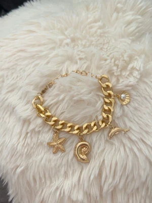 Guldigt armband med berlocker -  armband i guldfärgad med berlocker. 