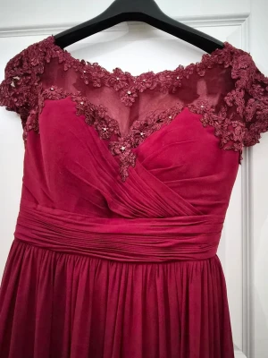 Vinröd långklänning med spetsdetaljer - Denna klänning kommer från det svenska märket LQ Design (Lilly Queen Design), som specialiserar sig på balklänningar och festkläder.Observera att klänningen ursprungligen är märkt som storlek EU 46, men den har blivit proffsigt ändrad/insydd till en storlek M. Den sitter därför som en storlek M idag.