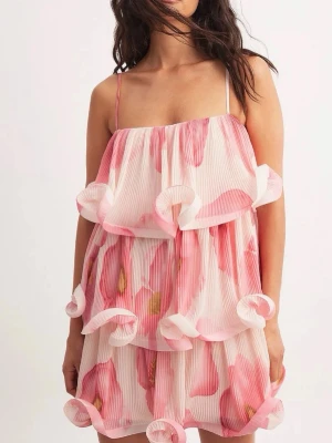 Blommig volangklänning med tunna band - Supersöt kort klänning med rosa och vita blommor, tunna axelband och flera lager volanger. Plisserat tyg ger extra struktur och volym. Perfekt för sommarens alla tillfällen och ger en lekfull vibe.