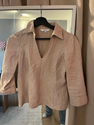 Beige skjortblus  med v-ringning - Snygg beige skjorta med v-ringning och diskret mönster. Skjortan har trekvartsärm och klassisk krage. Vintage från märket petite collection. Storlek 36 