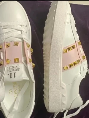 Vita Valentino sneakers med nitar - LÅNAD BILD! Kan skicka vanlig om de frågas! Skriv innan ni köper tack! Snygga valentino skor med rosa band och guldiga nitar. Skorna har en chunky sula och coola detaljer längs sidorna. Perfekta för dig som vill sticka ut med exklusiv design och trendiga inslag.
