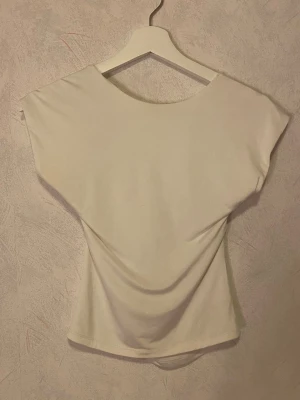 Vit satintopp med öppen rygg - Snygg vit satintopp med korta ärmar och en unik öppen rygg med draperad detalj. Toppen har en mjuk, stretchig passform och är perfekt för dig som vill ha något stilrent men ändå speciellt. Passar till många olika looks och är lätt att matcha. Storlek M från Stradivarius🤍knappt använd