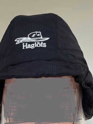 Svart mountain cap Haglöfs Stl S unisex Nyskick - Unisex. Svart Haglöfs mössa med Activent-teknologi. sportmössa. unisex, designad för vandring, friluftsliv och topptur. Denna mössa ger pålitlig värme och skydd mot väder och vind under kalla dagar utomhus. Mountain Cap är en Haglöfs-klassiker, mångsidigt väderskydd under alla typer av äventyr. dubbelvävt skalmaterial som effektivt står emot vind och fukt, samtidigt som det behåller god andningsförmåga. Insidan är fodrad med mjuk pilefleece för att ge skön värme och komfort, enkelt kan fälla upp