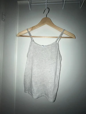 Ljusgrå linnetopp med smala band - En enkel och stilren ljusgrå linnetopp med smala axelband. Toppen har en rak passform och är tillverkad i mjukt bomullsmaterial, perfekt för varma dagar eller som lager under andra plagg.