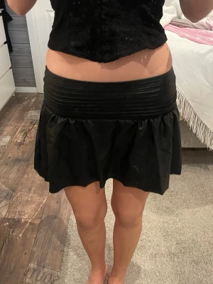 Svart kortkjol med volang - Säljer en svart kortkjol med bred midjeresår och volang nedtill. Kjolen har en enkel och stilren design som passar till många olika outfits. Materialet känns mjukt och följsamt, perfekt för dig som gillar en trendig och bekväm look. Strl 146/152 men passar mig som har xs och är 165 cm!