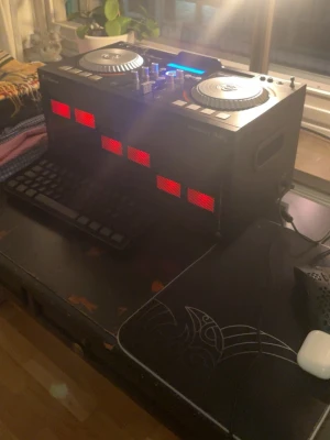 iDance DJ-mixer Energy XD3 med ljus - Säljer en svart DJ-mixer från iDance, modell Energy XD3. Den har två stora silverfärgade jog wheels, flera reglage och knappar samt en digital display med blå bakgrundsbelysning. Framsidan har röda LED-lampor. Perfekt för dig som vill mixa musik hemma.