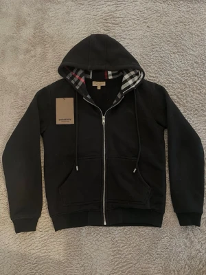 Burberry Zip up - Svart Burberry zip up hoodie i bra skick (använt regelbundet de senaste 4-5 månaderna) i storlek S, men passar lite som XS/S blandning. Insidan är otroligt mjuk och ut av bra material. Kommer med dust bag samt tags. Skriv gärna på vid undringar eller pris förslag då priset ej är suttet! 🙏💬  Obs: Den ser dammig ut på bilderna eftersom att den legat i garderoben, det går bort enkelt.