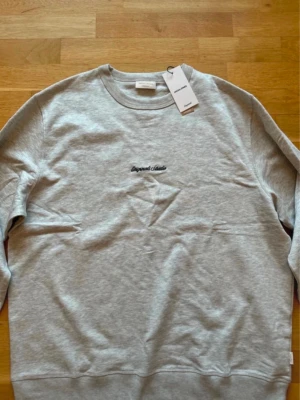 Grå sweatshirt från Jack & Jones - Snygg grå sweatshirt från Jack & Jones med broderad text 'Originals Studio' på bröstet. Tröjan har rund halsringning och är tillverkad i mjuk bomullsmix. Perfekt för en avslappnad och stilren look.