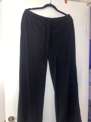 Svarta vida leggings med dragsko - Säljer ett par svarta leggings med vida ben och dragsko i midjan. De har en avslappnad passform och är perfekta för en chill och bekväm stil. Materialet känns mjukt och stretchigt, vilket gör dem sköna att ha på sig hela dagen.