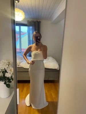 Vit axelbandslös långklänning - Säljer denna superfina eleganta vita balklänning från Jarlo London. Klänningen är i storlek UK6, XS, och är använd en gång. Klänningen har ett litet släp och passar perfekt till bal. Finns små defekter längs ut på släpet (efter att den släpat i marken), bilder kan skickas vid önskan. Nypris 2000kr💕