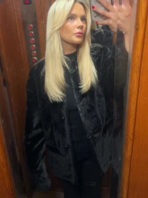 Svart pälsjacka med knappar - Kostar 2600kr ny och är helt oanvänd ! Säljer en svart pälsjacka med klassisk passform och stora knappar framtill. Jackan har en mjuk och glansig yta som ger en lyxig känsla. Perfekt för att hålla sig varm under kalla dagar. Materialet är syntetpäls och jackan har långa ärmar.