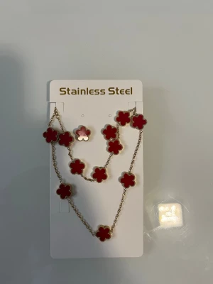Halsband med röda blommor i stål - Snyggt halsband i rostfritt stål med flera röda blommor i emaljdesign. Blommorna har guldfärgade kanter och sitter på en tunn guldfärgad kedja. Perfekt för dig som vill ha en färgklick till din outfit.