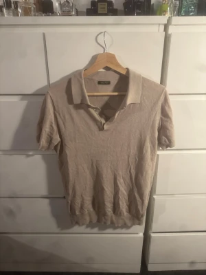 Beige polotopp från Italien - Säljer en stilren beige polotopp köpt i Italien för ca 900 med klassisk krage och korta ärmar. Toppen har knappar vid halsen och är tillverkad i ett mjukt material som känns skönt mot huden. Perfekt för dig som gillar en clean och enkel look.