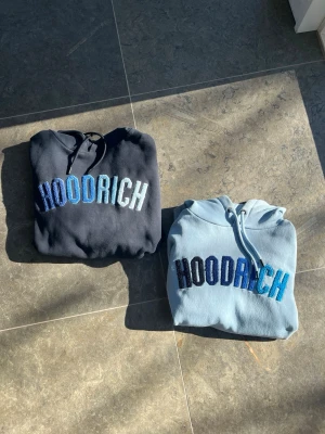 BUNDLE 2 Hoodrich hoddies Storlek S OCH M - Två snygga hoodies från Hoodrich, en i mörkblått och en i ljusblått. Båda har stor broderad HOODRICH-logga i olika blå nyanser på bröstet och klassisk huva med dragsko. Perfekta för en chill och trendig streetwear-look. De är i fint skick men den ljusblåa har två små röda fläckar som tuyvärr ej går bort annars är allt som det ska. Hör av er om ni har frågor. OBS den mörkblåa är i storlek M och den ljusblåa är i storlek S!!!