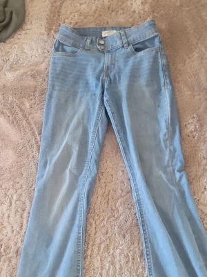 Ljusblå jeans med fjärilsdetalj - Säljer ett par ljusblå jeans från Lindex med en snygg fjärilsdetalj på bakfickan. Jeansen har klassisk femficksmodell, raka ben och är gjorda i mjukt denimtyg. Perfekta för dig som gillar unika detaljer och en avslappnad stil.