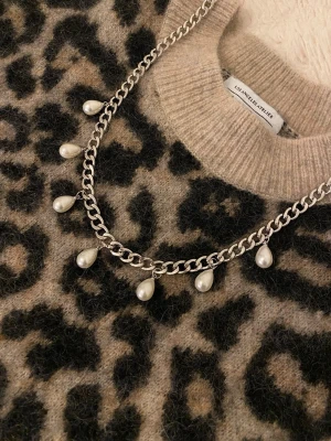 Silverfärgat halsband med droppformade pärlor - Snyggt halsband i silverfärgad rostfritt stål med sju droppformade vita pärlor som hänger längs kedjan. Perfekt för att ge en trendig touch till din outfit.