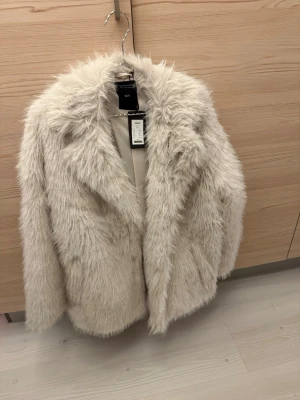 Fuskpäls jacka från lager157 - Fuskpäls jacka från lager 157. Strl XS/S. Vit/grå/beige färg. Två fickor samt två ”osynliga” knappar för att stänga jackan. Otroligt snygg jacka, perfekt till våren! 