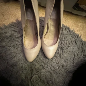 Beige klassiska pumps med spetsig tå - Snygga pumps i beige med spetsig tå och hög klack. Skorna har en stilren design och är tillverkade i ett material med lätt glans. Perfekta för dig som gillar en elegant och tidlös look.