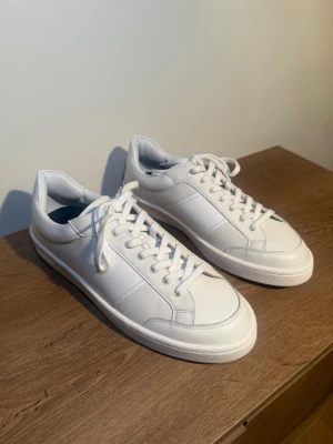 Vita sneakers i läder från Sandro  - Ett par vita stilrena sneakers från Sandro! Som med sina detaljer på sidan gör att skon sticker ut bland vita Sneakers!