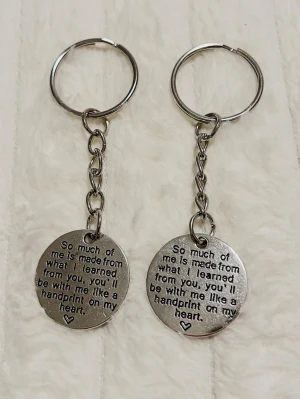 Nyckelringar med graverad text - Två runda nyckelringar i silverfärgad metall med graverad text: 'So much of me is made from what I learned from you, you'll be with me like a handprint on my heart.' Perfekt som personlig accessoar eller present.