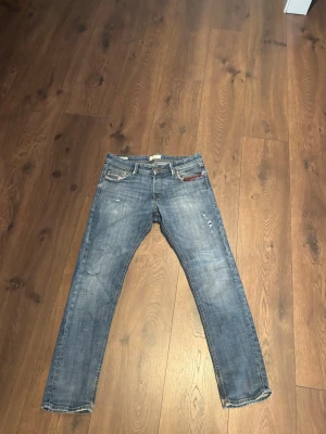 Blå raka jeans från Jack and Jones - Säljer ett par blå jeans från Jack and Jones (slim/glennin) med raka ben och slitna detaljer. Jeansen har klassisk femficksdesign, synliga nitar och en liten röd detalj vid fickan fram. Materialet är denim i bomull med en tvättad look. De har ett litet hål men syns inte när du bär dom.31 x 30