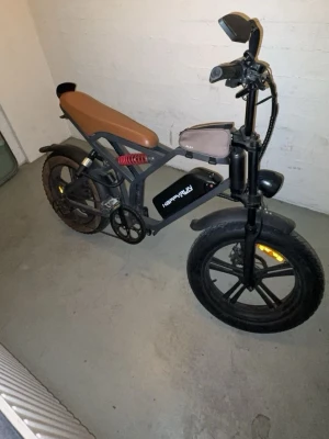 Svart Happyrun elcykel med brunt säte - Elcykel från Happyrun i svart med brunt, avlångt säte. Cykeln har breda däck, robust ram i metall, stötdämpare bak och spegel på styret. Batteriet sitter monterat på ramen och cykeln har både skärmar och kedjeskydd. Perfekt för dig som gillar eldrivna fordon med cool design.