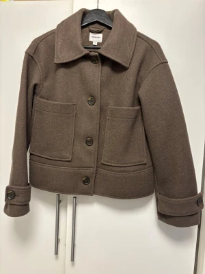 Brun jacka från Kappahl XS (passar både S och mig som är M) - Kort brun jacka från Kappahl. Jackan har stora framfickor, bred krage, knappar framtill och på ärmsluten. Perfekt oversized look med raka linjer och enkel design som passar till många outfits.