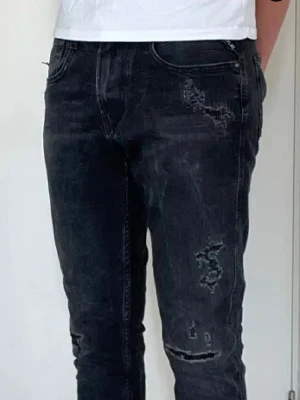 Svarta slitna jeans från Replay - Säljer ett par svarta jeans från Replay med snygga slitningar och distressed detaljer på benen. Modellen är smal och har klassisk femficksdesign. Perfekta för en cool och avslappnad stil. Materialet är bomull med stretch för extra komfort.