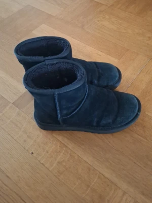 Svarta korta boots i mocka - Mysiga svarta boots i mocka med kort skaft och mjukt foder på insidan. Perfekta för kalla dagar när du vill ha både stil och komfort. Klassisk design med rund tå och diskreta sömmar. Passar till det mesta i garderoben.