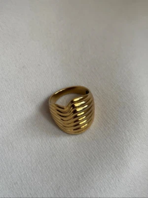Guldfärgad ring från Edblad - Snygg guldfärgad ring från Edblad med vågformad, ribbad design. Storlek M (17,5 mm). Mycket fint skick.