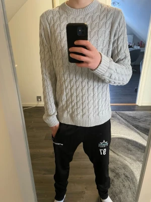 Ljusgrå kabelstickad tröja - Säljer en ljusgrå kabelstickad tröja med rund halsringning och ribbade muddar vid ärmslut och nederkant. Tröjan har ett klassiskt flätmönster och är perfekt för dig som gillar en stilren och enkel look. Passar till både jeans och chinos. Tröjan är från only&sons och priset kan diskuteras 