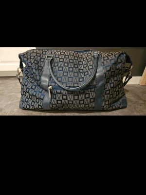 Blå weekendbag med mönster - Weekendbag från Vezzano.  I det stora hela är väskan i gott skick. Fästena för axelremmen är lite slitna, var god se bilder!  Inte använd senaste ca 6 åren.