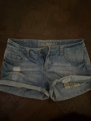 Ljusblå jeansshorts från Fishbone - Snygga ljusblå jeansshorts från Fishbone med upprullade benslut och slitna detaljer. Klassisk femficksmodell med knappgylf och bälteshällor. Perfekta för varma dagar och enkel att matcha med olika toppar. Är mellan S och Xs i storlek skulle jag säga! 