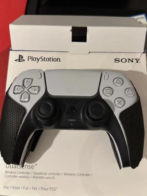 PlayStation 5 DualSense handkontroll - Säljer en PlayStation 5 DualSense handkontroll från Sony. Kontrollen är vit med svarta detaljer och har texturerade grepp i svart gummi för extra komfort. Den har klassisk PlayStation-design med touchpad, adaptiva triggers och inbyggd mikrofon.