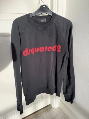 Svart sweatshirt från Dsquared2 - Stilren svart sweatshirt från Dsquared2 med röd logotyp på bröstet. Tröjan har rund halsringning, långa ärmar och ribbade muddar vid ärmslut och nederkant. Perfekt för en avslappnad look.