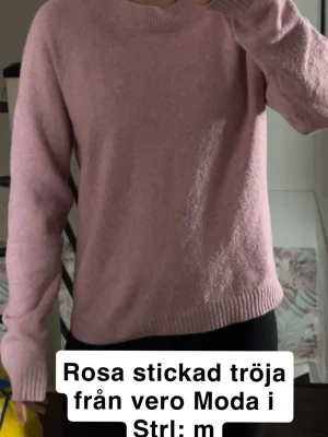 Rosa stickad tröja från Vero Moda - Mysig rosa stickad tröja från Vero Moda i storlek M. Tröjan har rund halsringning, långa ärmar och ribbade muddar vid ärmslut och nederkant. Perfekt för att hålla värmen under kyliga dagar och enkel att matcha med olika outfits. 