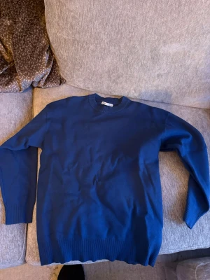 Blå stickad tröja med rund hals - En stilren blå stickad tröja med rund halsringning och ribbade muddar vid ärmslut och nederkant. Perfekt att matcha med jeans eller kjol för en enkel och snygg look.