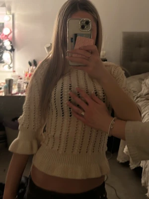 Beige croppad stickad tröja - Säljer en beige croppad stickad tröja med trekvartsärm och ribbade detaljer. Funkar bäst med vit bh. Tröjan har ett hålmönster över hela och volangkant nedtill samt vid ärmslut. Perfekt för dig som gillar en chill och trendig stil.