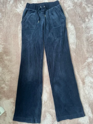 Mörkblåa Juicy Couture byxor!! - Mjukisbyxor i mörkblå velour med bred resår i midjan och dragsko. Byxorna har två stora framfickor och två bakfickor med knappdetaljer. Rak passform och sköna att ha på sig. Perfekta för en avslappnad stil.