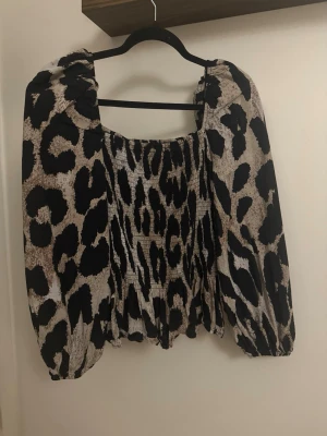 Leopardmönstrad blus med puffärm - Trendig blus med leopardmönster i beige, svart och brunt. Blusen har fyrkantig ringning, puffiga långärmar och smockad kropp för en snygg passform. Tillverkad i ett lätt och luftigt material som ger en cool look.
