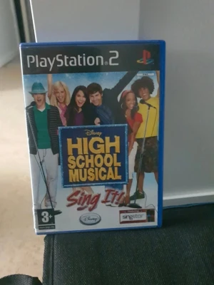High School Musical Sing It! PS2 - High School Musical Sing It! till PlayStation 2 är ett karaoke-spel där du sjunger med till låtar från High School Musical-filmerna. Spelet kommer i ett blått plastfodral med färgglad framsida och är kompatibelt med SingStar-mikrofoner.