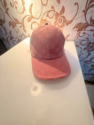 Rosa keps - Säljer en snygg rosa keps med det klassiska GG-monogrammet över hela kepsen. Kepsen är i tygmaterial och har justerbar rem baktill. Perfekt accessoar för att lyfta din outfit med en lyxig touch.
