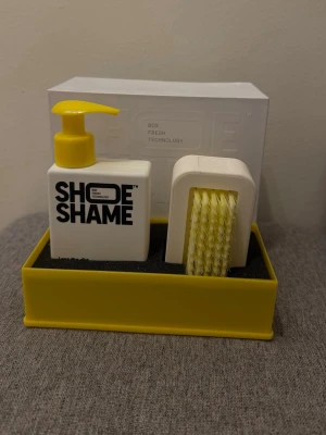 Skorengöringskit  - Shoe Shame Lose the dirt Kit innehåller 150 ml rengöringsgel och en dubbelsidig borste. Perfekt för att hålla sneakers och andra skor fräscha. Snygg design i vitt och gult, enkel att använda och passar alla typer av material.