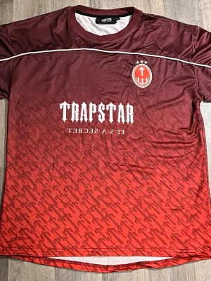 Trapstar football jersey - Säljer denna snygga limited editon t-shirt från Trapstar i röd och vinröd ton med vit logga och text framtill. Tröjan har ett sportigt tryck med siffran 22 på ryggen. Storlek S men passar nog också M-L, köpte den cirka 1-2 år sen men glömde bort att jag hade den och ej använd.