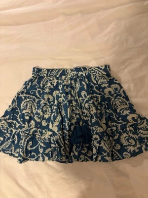 Blåvit kortkjol med volang och knyt - Supersöt kortkjol i blått och vitt med blommigt mönster. 